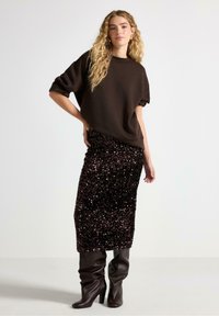Brun oversized sweatshirt med korta ärmar, kombinerad med en knälång svart paljettkjol och knähöga bruna klackstövlar.