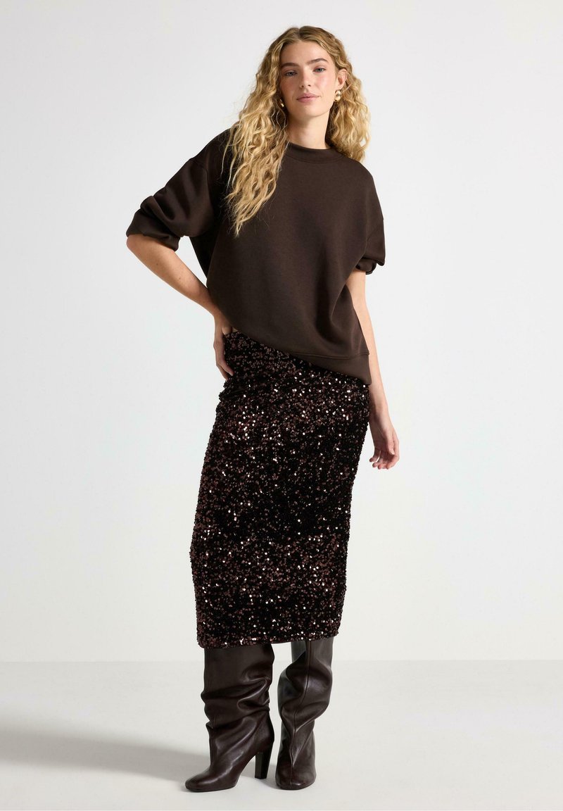 Brun oversized sweatshirt med korta ärmar, kombinerad med en knälång svart paljettkjol och knähöga bruna klackstövlar.