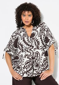 Blouse à motifs marron et blanc avec un encolure en V, manches courtes avec des détails à nouer, et une silhouette fluide. Fabriquée en tissu léger.