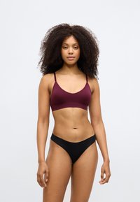 Bralette borgonha com alças ajustáveis, combinado com cuecas de biquíni pretas. Textura suave e design minimalista, sem hardware visível.