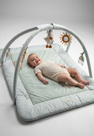 Baby lying on light green play mat with padded arches and hanging soft toys including a bird and sun with mirror.