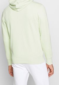 Světle zelená mikina s kapucí, která má prostornou kapuci, žebrované manžety a lem; vyrobená z měkké, strukturované bavlněné tkaniny.