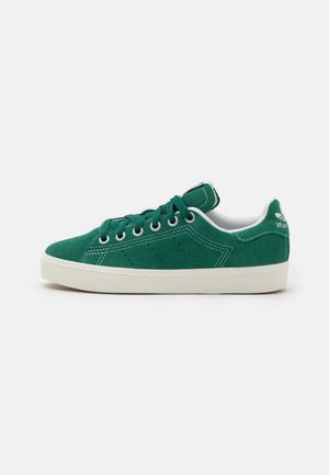 Niski zielony zamszowy sneaker z białą podeszwą, zielonymi sznurowadłami i białym przeszyciem, widziany z boku na jednolitym tle.