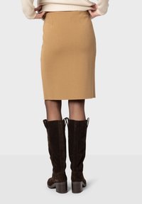 Jupe crayon slim en couleur camel, fabriquée en tissu doux avec une texture lisse. Associée à des bottes en daim marron foncé hauteur genou.