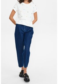 Witte T-shirt met korte mouwen en meerkleurige stippen, gecombineerd met hooggeplaatste donkerblauwe spijkerbroek en zwarte schoenen met gouden hardware accentueringen.