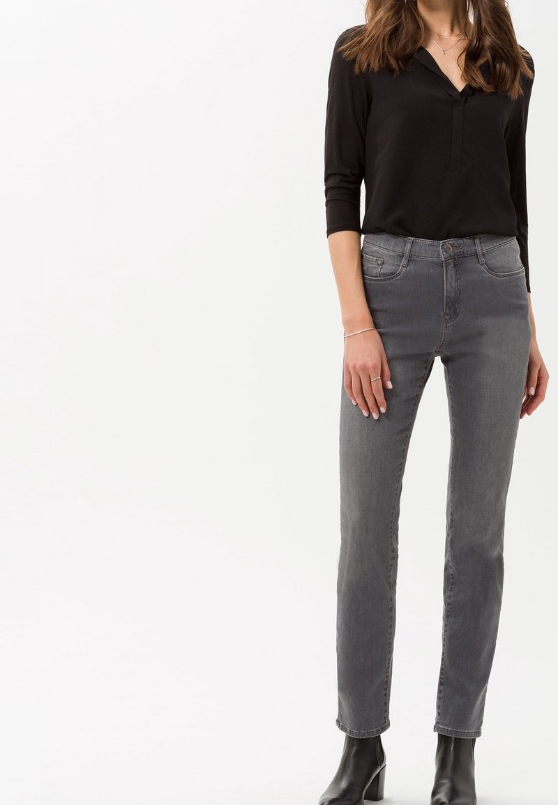 Jeans grises con un corte recto, diseño de cinco bolsillos y un desvanecimiento sutil. Combinados con una camisa negra de manga larga con botones.