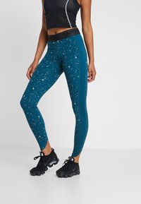 Leggings teal con un patrón moteado, que cuentan con una cinturilla negra con la marca "Nike Pro" y un diseño de ajuste ceñido.