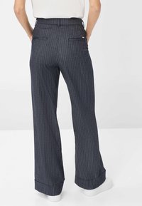 Pantalons à jambe large en tissu à rayures foncées, avec une taille haute, des poches arrière doubles et des poignets retroussés. Associés à des baskets blanches.