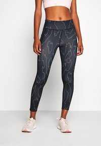 Leggings noirs avec un motif abstrait subtil, taille haute et tissu extensible. Portés avec des baskets légères à accents roses.