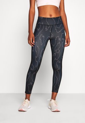 Leggings noirs avec un motif abstrait subtil, taille haute et tissu extensible. Portés avec des baskets légères à accents roses.