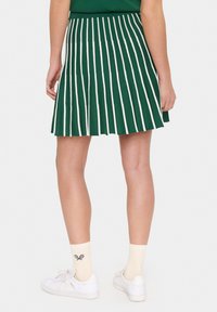 Jupe plissée verte avec des rayures verticales blanches, dotée d'une taille ajustée. Associée à des baskets blanches et des chaussettes crème au motif de raquette de tennis.