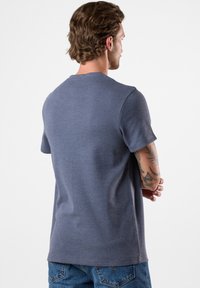 T-shirt grigia a girocollo in tessuto lavorato, maniche corte e vestibilità comoda, vista da dietro con jeans in denim.