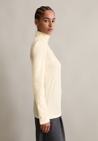 Long-sleeve, light yellow turtleneck top made of soft fabric, fitted design, smooth texture, paired with a plaid skirt.