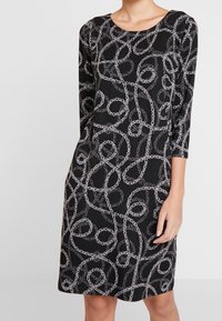 Vestito nero con motivo a catena in argento, con maniche a tre quarti e scollatura tondeggiante, lunghezza fino al ginocchio, in tessuto morbido.