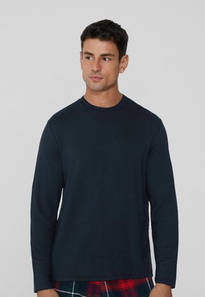 Navyblaues Langarmshirt aus weichem Stoff, mit Rundhalsausschnitt und geradem Saum. Kombiniert mit karierter Freizeit-Hose.