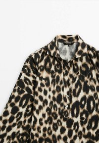 Chemise à manches longues imprimé léopard avec col, deux boutons sur le devant, et un mélange de taches noires, brunes et beiges sur le tissu.