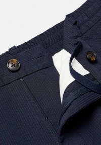 Pantalon bleu marine texturé avec fermeture par bouton, braguette zippée et doublure intérieure blanche visible au niveau de la ceinture.