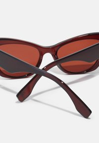 Retro kat-oog zonnebril met kastanjebruine glazen, een glanzend frame en slanke, gebogen armen. Opvallend door hun puntige uiteinden en donkere kleur.