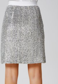 Mini-jupe en sequins argentés avec une taille lisse blanche. Les sequins créent un motif texturé et scintillant sur tout le tissu.