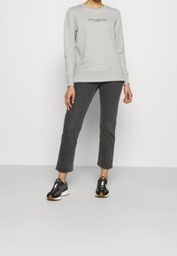 Grå sweatshirt med rund halsringning och "Tommy Hilfiger"-logotyp. Matchad med mörkgrå avklippta jeans och svarta sportskor.