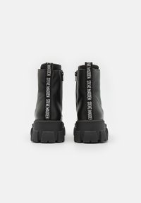 Botas de cuero negras hasta el tobillo con suelas de goma gruesas, cremalleras laterales y un detalle de logo en contraste en las lengüetas traseras.