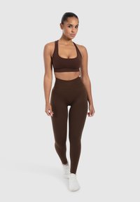 Bruine sportbeha en hooggeplaatste leggings in een bijpassende kleur, met een gladde structuur en een nauwsluitend ontwerp. Witte sportschoenen.