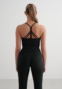 Zwarte sportkleding met een geribbelde textuur. De cropped top heeft een ontwerp met spaghettibandjes op de rug, terwijl de high-waisted leggings de getailleerde vorm benadrukken.