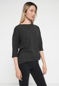 Tmavě šedý, oversized top s tříčtvrtečními rukávy a lodičkovým výstřihem, vyrobený z měkké, texturované tkaniny, kombinovaný s černými přiléhavými kalhotami.