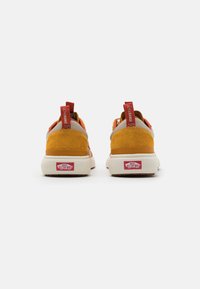 Ett par senapsgula och beige Vans Ultrarange sneakers visade från baksidan på vit bakgrund.