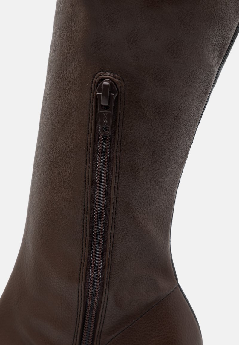 Nahaufnahme eines dunkelbraunen Lederstiefels mit einem vertikalen, dunkelbraunen Reißverschluss vor einem strukturierten Lederhintergrund.