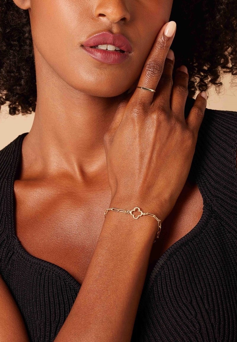 Gouden armband met een bloemmotief, met een schakelkett ontwerp. Draagt op een hand, tegen een zwart textuur top. Gladde afwerking.