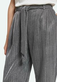 Metallic graue weit geschnittene Hose mit vertikalen Nadelstreifen und einem gebundenen Gürtel. Der Stoff hat einen strukturierten Glanz mit schimmernden Akzenten.