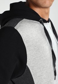 Felpa con cappuccio caratterizzata da un design a blocchi di colore in nero, grigio e grigio chiaro. Realizzata in tessuto morbido con coulisse e accenti testurizzati.