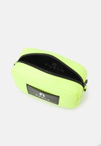 Neonově zelená obdélníková taštička s černým zipem a nášivkou loga Furla, částečně otevřená, ukazující černý interiér s brandingem Furla.