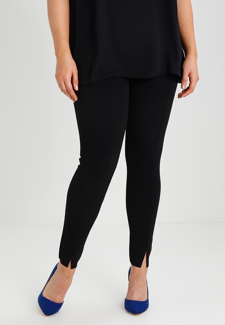 Leggings noirs à la coupe ajustée, avec des fentes sur les chevilles. Associés à des chaussures à talons hauts bleues. Tissu à texture lisse.