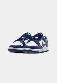 Navy and white leather sneakers feature perforated toe, laces, and a rubber sole. The design includes a logo on the tongue and side.