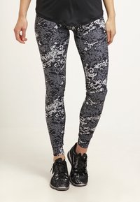 Legginsy w czarno-szare wzory z cyfrowym kamuflażem, wykonane z elastycznej tkaniny. Dobrane do czarnych butów sportowych.