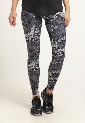 Leggings noirs et gris à motif camouflage numérique, fabriqués en tissu extensible. Associés à des chaussures de sport noires.