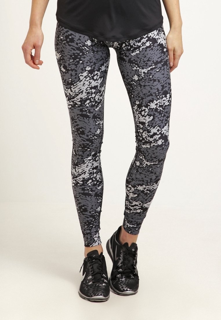 Legginsy w czarno-szare wzory z cyfrowym kamuflażem, wykonane z elastycznej tkaniny. Dobrane do czarnych butów sportowych.