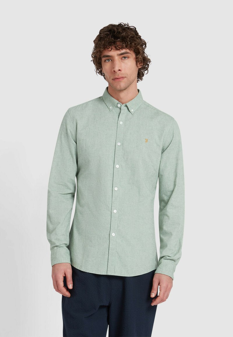 Lichtgroene shirt met lange mouwen in een gestructureerde stof, voorzien van een overhemdkraag en witte knopen, met een klein geborduurde logo op de borst.