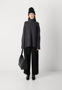 Pull en maille épaisse gris foncé avec un col haut, un ourlet côtelé et des manches évasées, associé à un pantalon large noir et un sac à épaule noir.