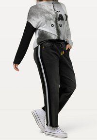 Suéter gris y negro con un estampado gráfico, combinado con pantalones negros con franjas laterales y cordón. Zapatillas blancas completan el conjunto.