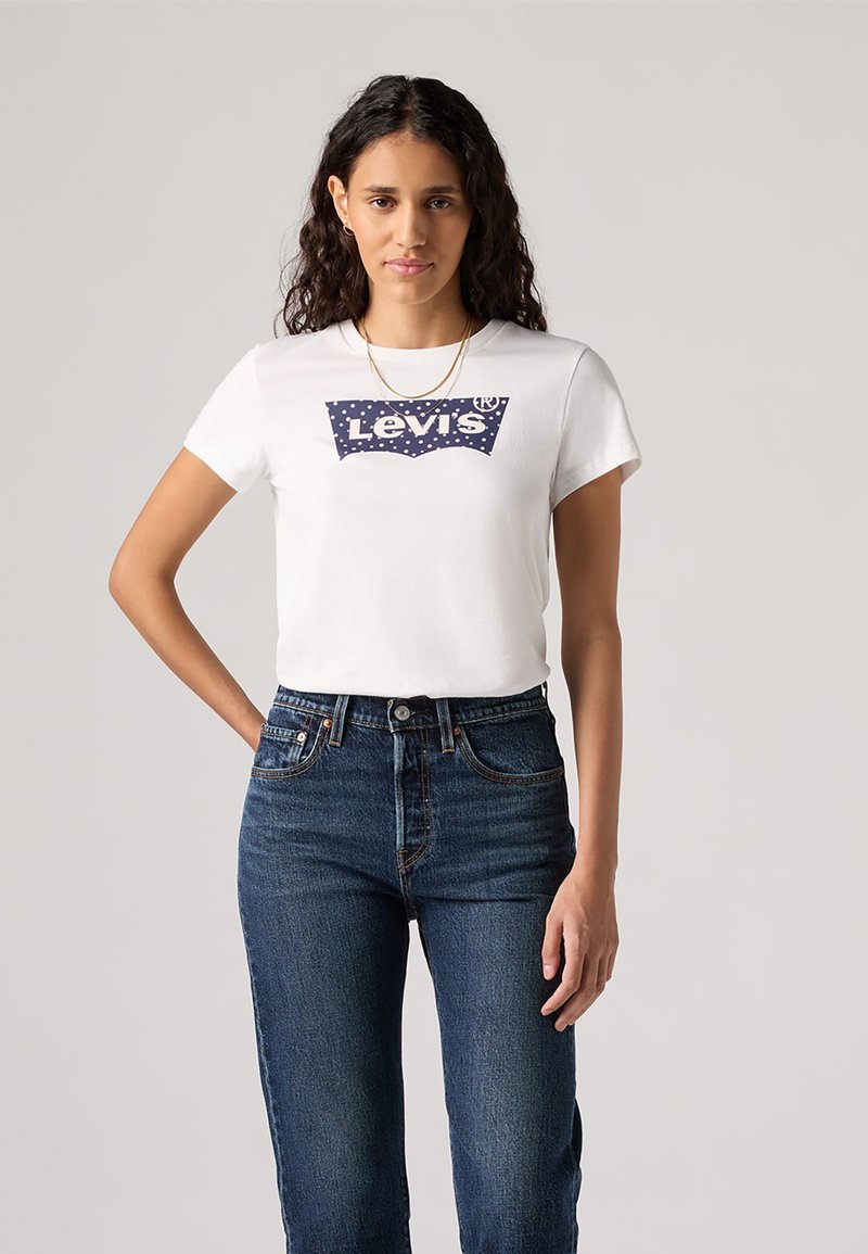 Balta medvilninė marškinėliai su tamsiai mėlynu Levi's logotipo raštu, dekoruotu taškeliais, derinami su tamsiai mėlynomis džinsinėmis aukštos talpos kelnėmis. Trumpomis rankovėmis, klasikinio kirpimo.