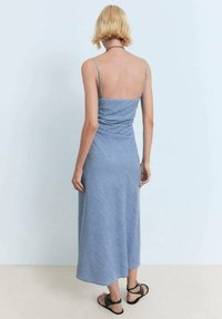 Denim-colored mid-length dress with thin straps, textured fabric, and a slightly flared hem, paired with black strappy sandals.