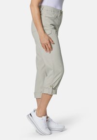 Hellgraue, taillierte Hose mit elastischem Bund, aufgerolltem Saum und seitlichen Taschen, kombiniert mit weißen Sneakern. Glatte Stofftextur.
