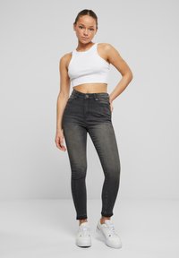 Crne skinny traperice visokog struka, izrađene od denima, s glatkom teksturom, prednjim džepovima i blagim gradijentnim ispiranjem. Uparene s bijelim cropped topom.