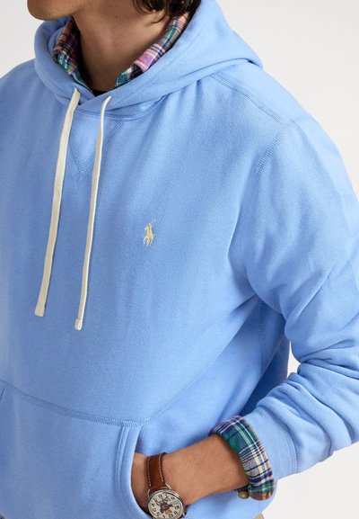 Σιέλ φούτερ με κουκούλα από βαμβάκι, με εμπρόσθια τσέπη, κουκούλα με κορδόνι και μικρό κεντημένο λογότυπο. Φαίνονται τα μανίκια καρό πουκάμισου.