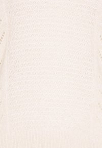 Krämfärgad stickad tröja med en lös struktur, med en ribbad nederkant och öppna vävdetaljer på ärmarna.