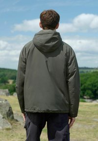 Jachetă cu capușon de un verde închis, cu o textură netedă și un design casual, având o croială lejeră și manșete elastice. Purtați-o cu pantaloni cargo negri.