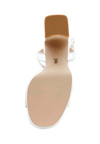 Hvide hælede sandaler med en glat, struktureret sål og tan gummielement. Har tynde stropper og et logoaccent nær hælens midte.